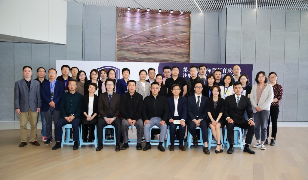 A group of people in formal and casual attire posing for a photo indoors, with a banner in the background.