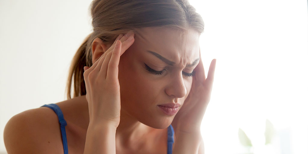 A woman pressing her temples with her fingers, appearing to have a headache.