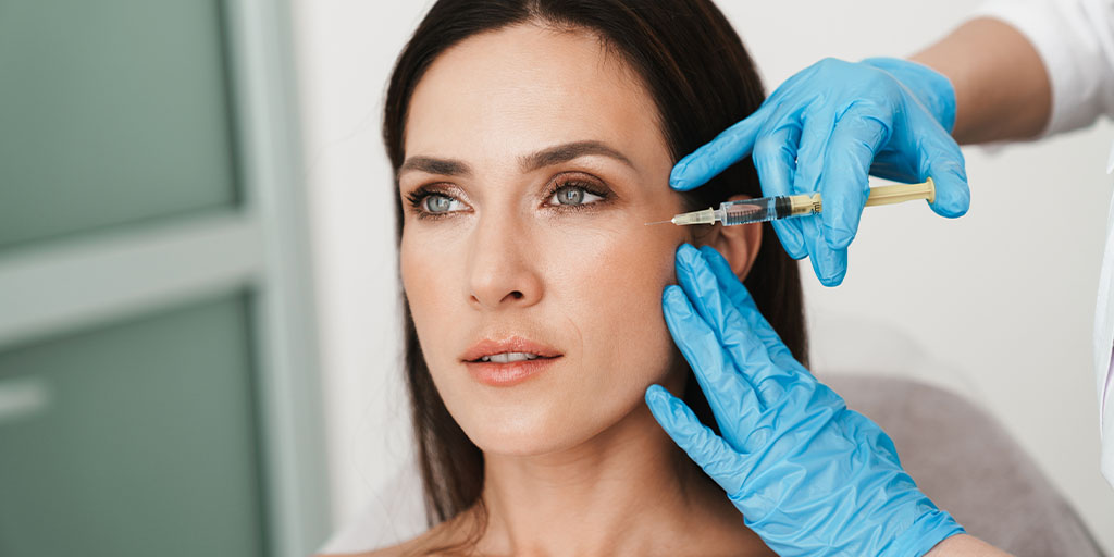 A person receives a facial injection from a medical professional wearing blue gloves.