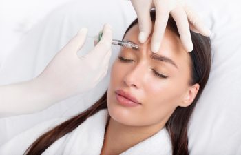 Young woman recieving injection of anti-aging botox filler to forehead from professional cosmetologist in beauty salon